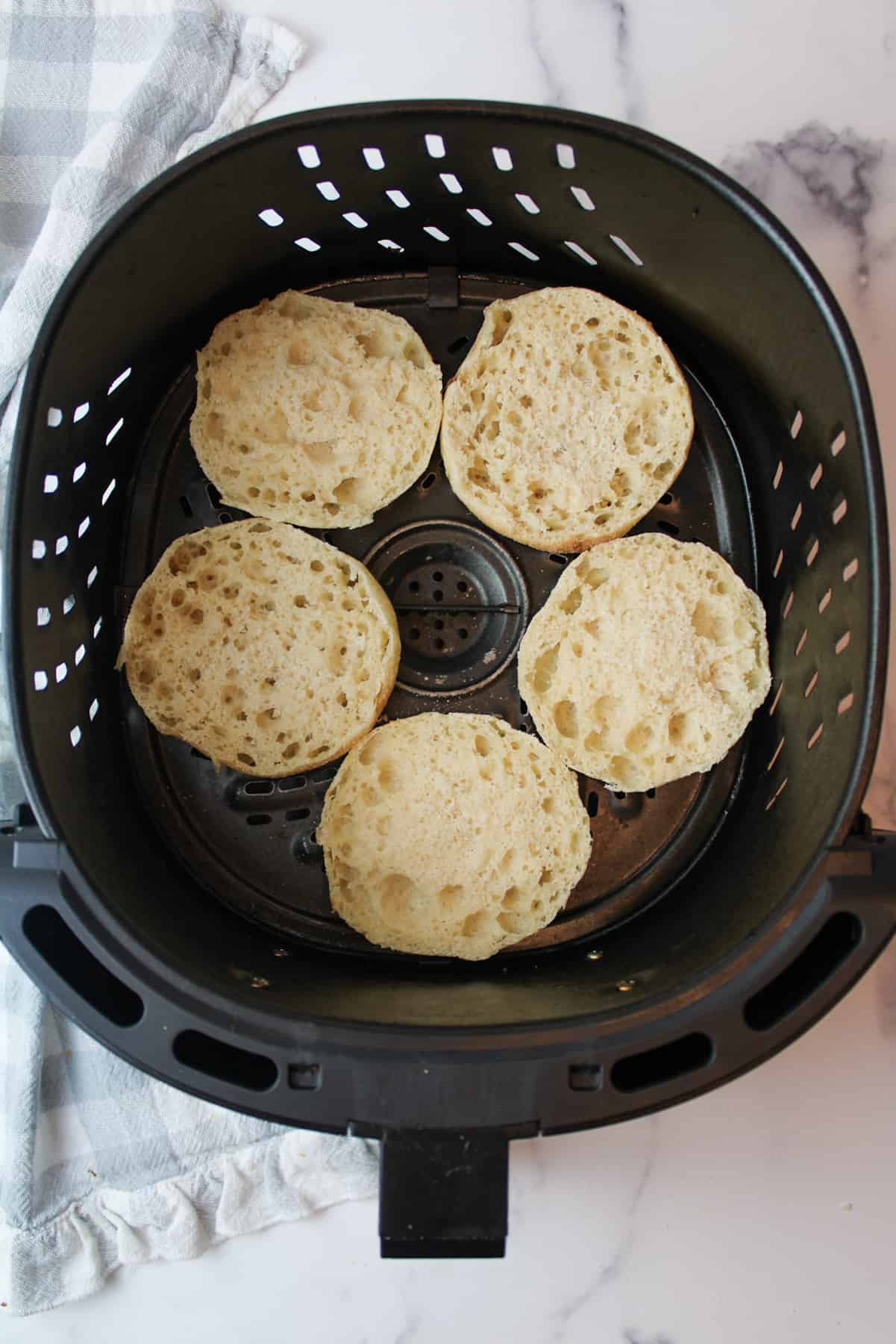 sliced english muffins in a air fryer basket.