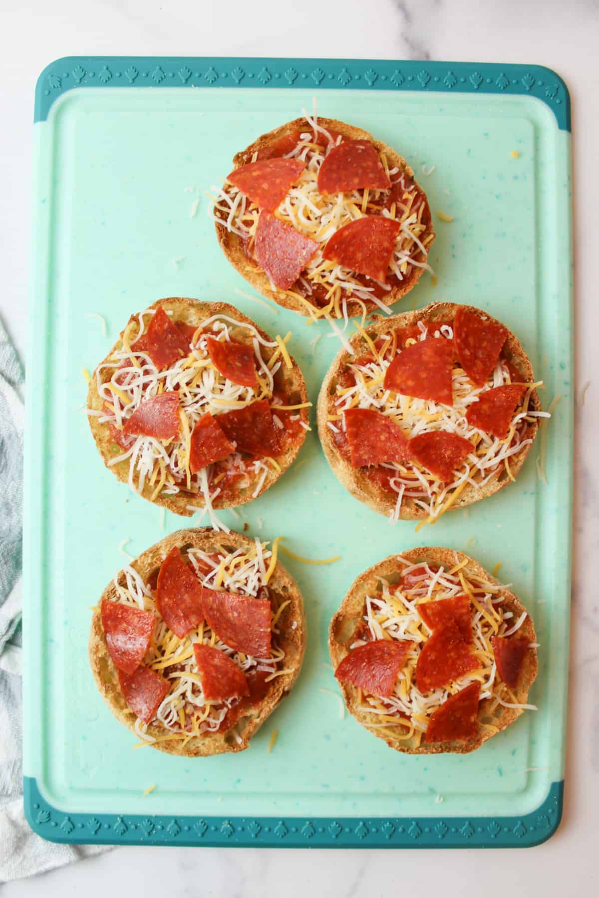 assembled and unbaked english muffin pizzas on a cutting board
