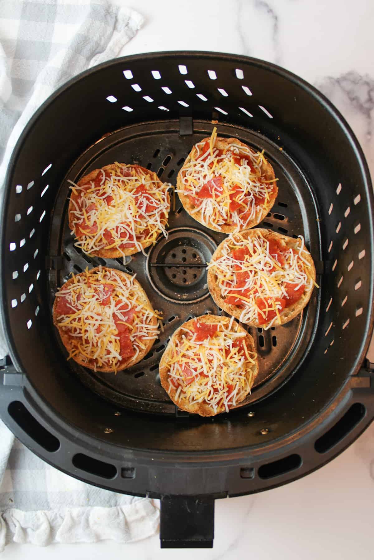 uncooked english muffin pizzas in an air fryer basket