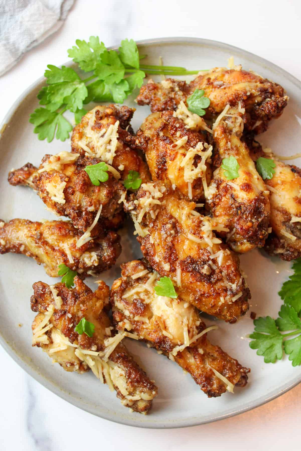 garlic parmesan chicken wings on a plate with green herb garnish.