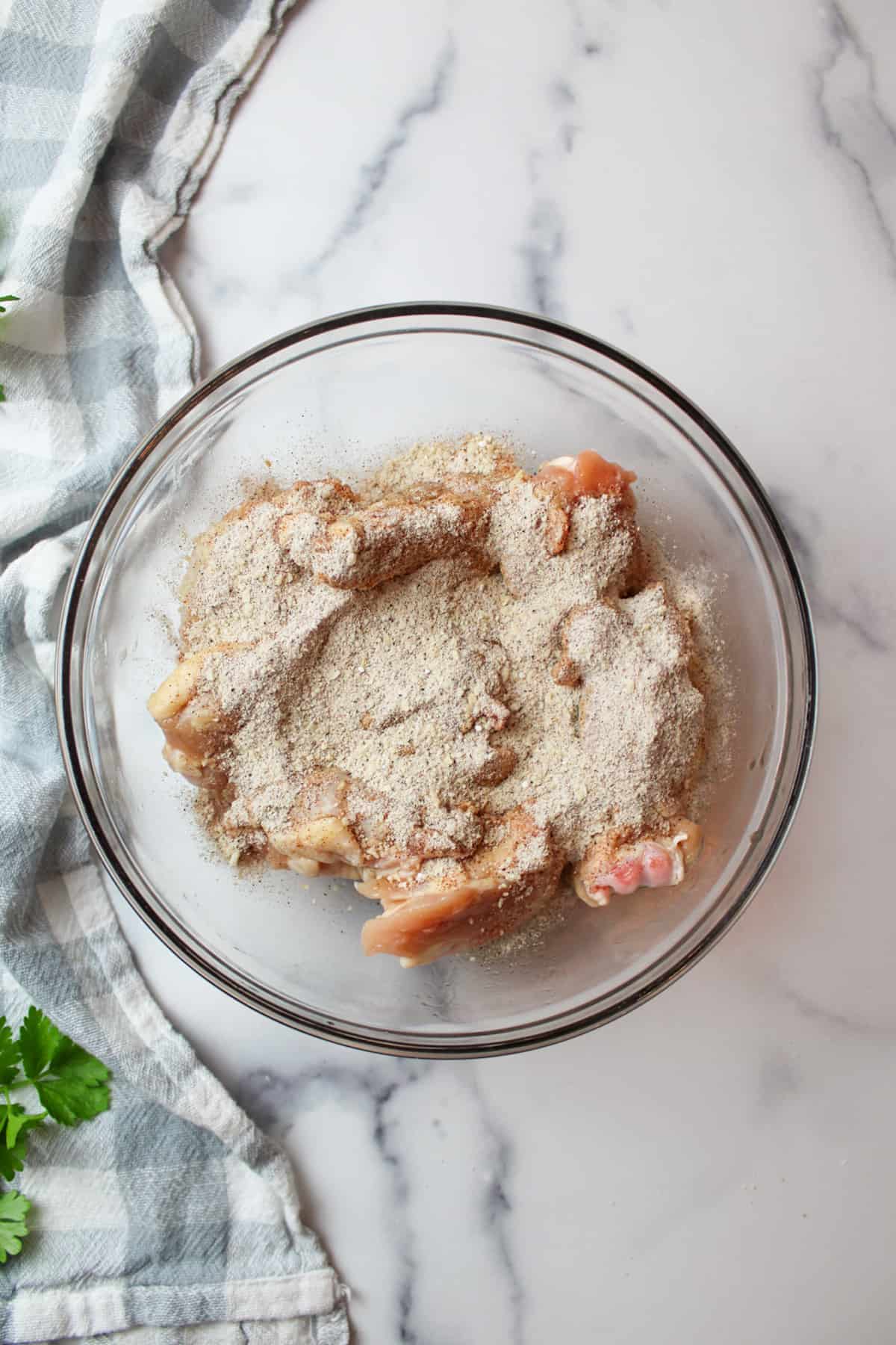 parmesan cheese seasoning mixture over raw chicken wings in a mixing bowl.