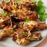 garlic parmesan chicken wings on a plate with green garnishes.
