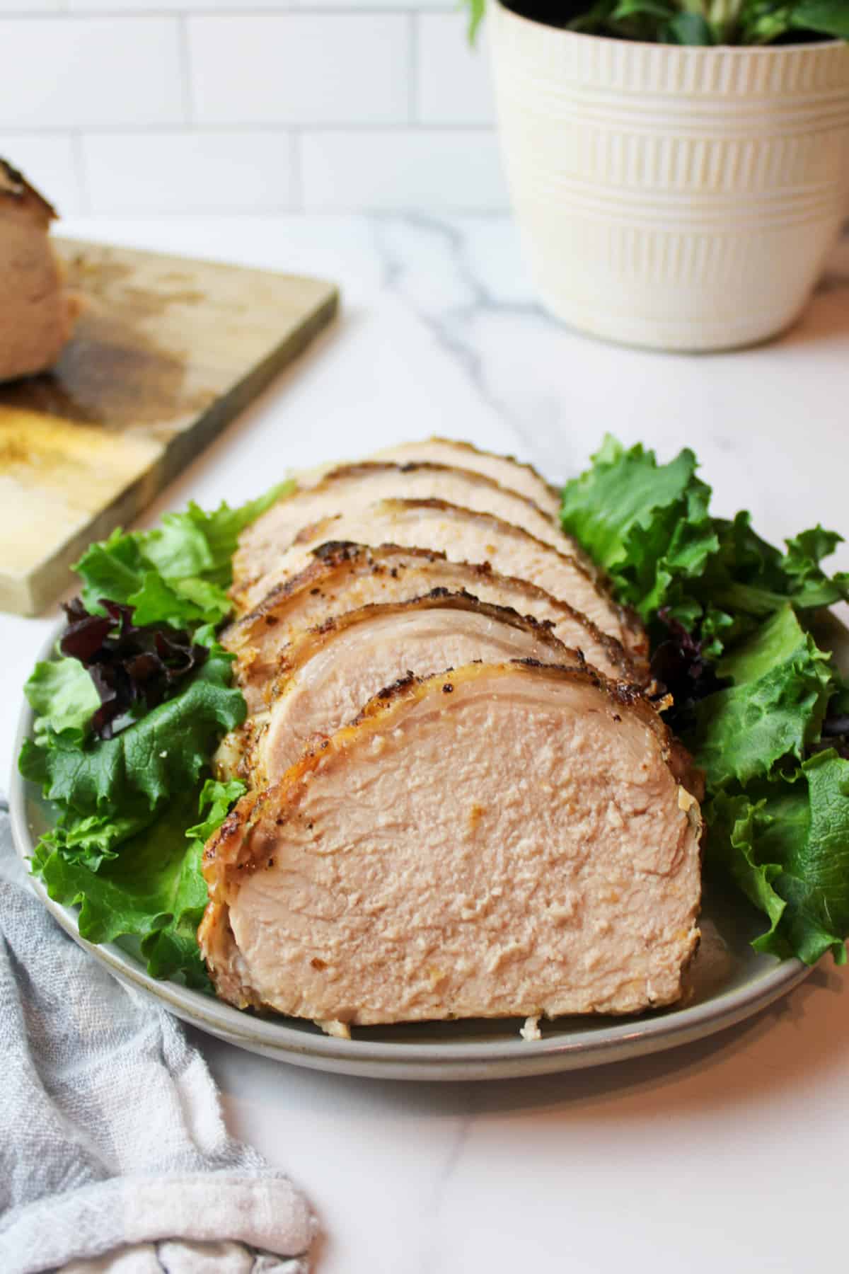 a sliced air fried pork loin on a plate with green leaf lettuce on the sides