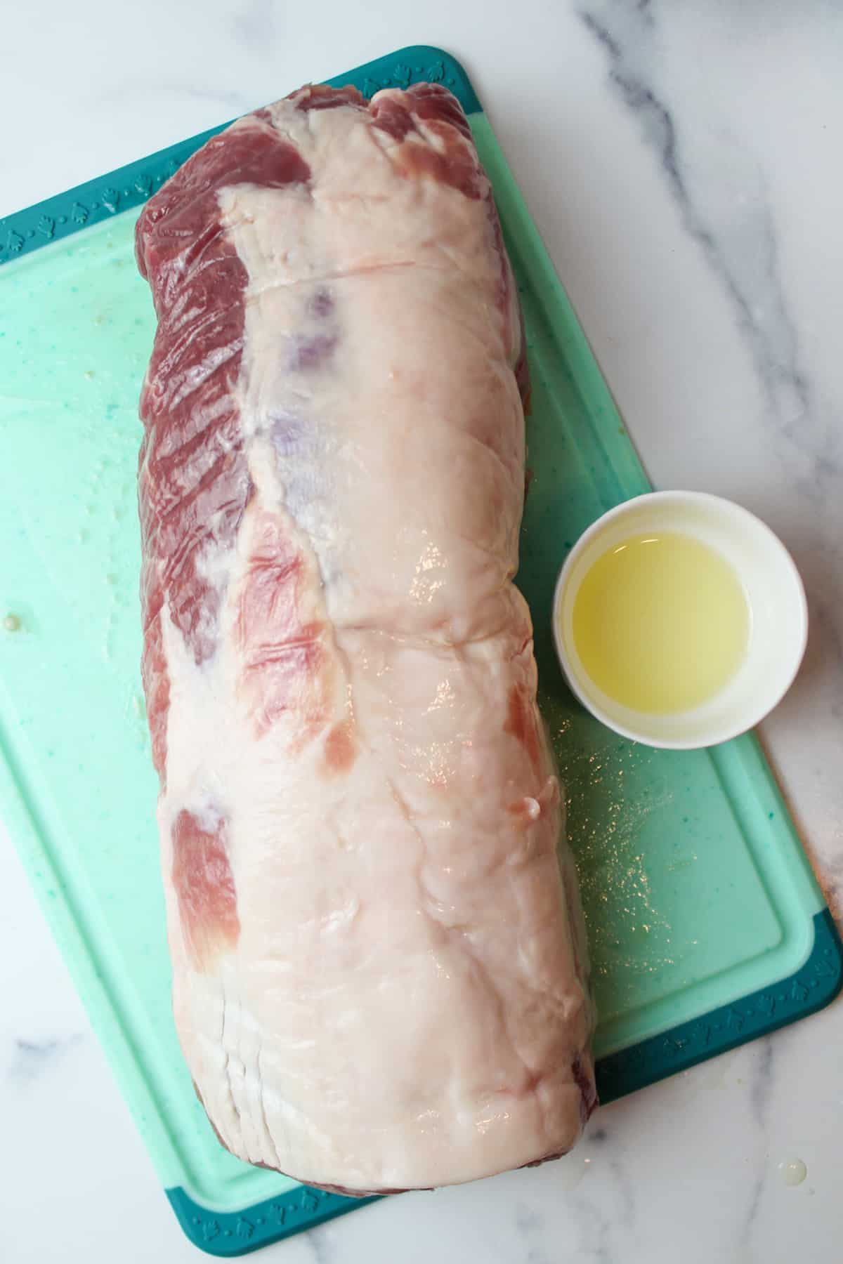 Pork loin on cutting board with olive oil, bowl of oil aside.