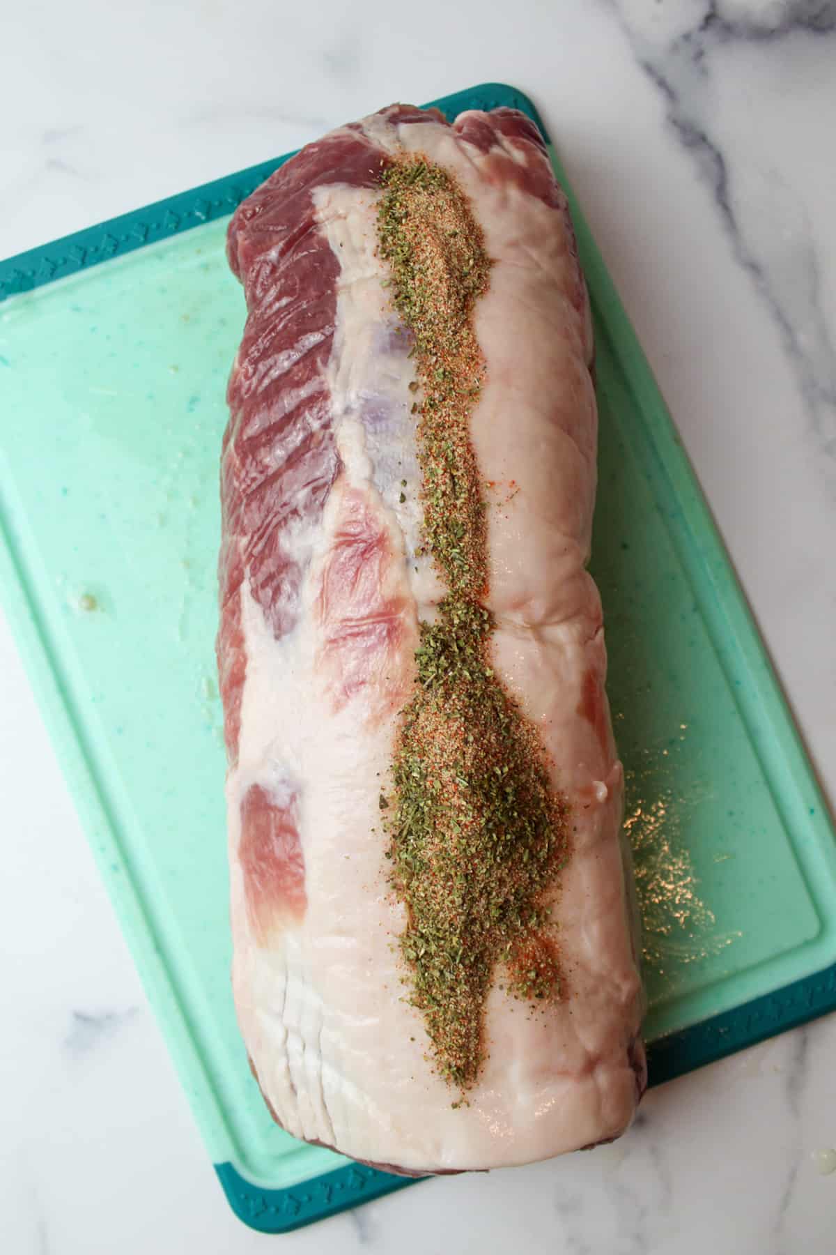 seasoning topped pork loin on a cutting board.