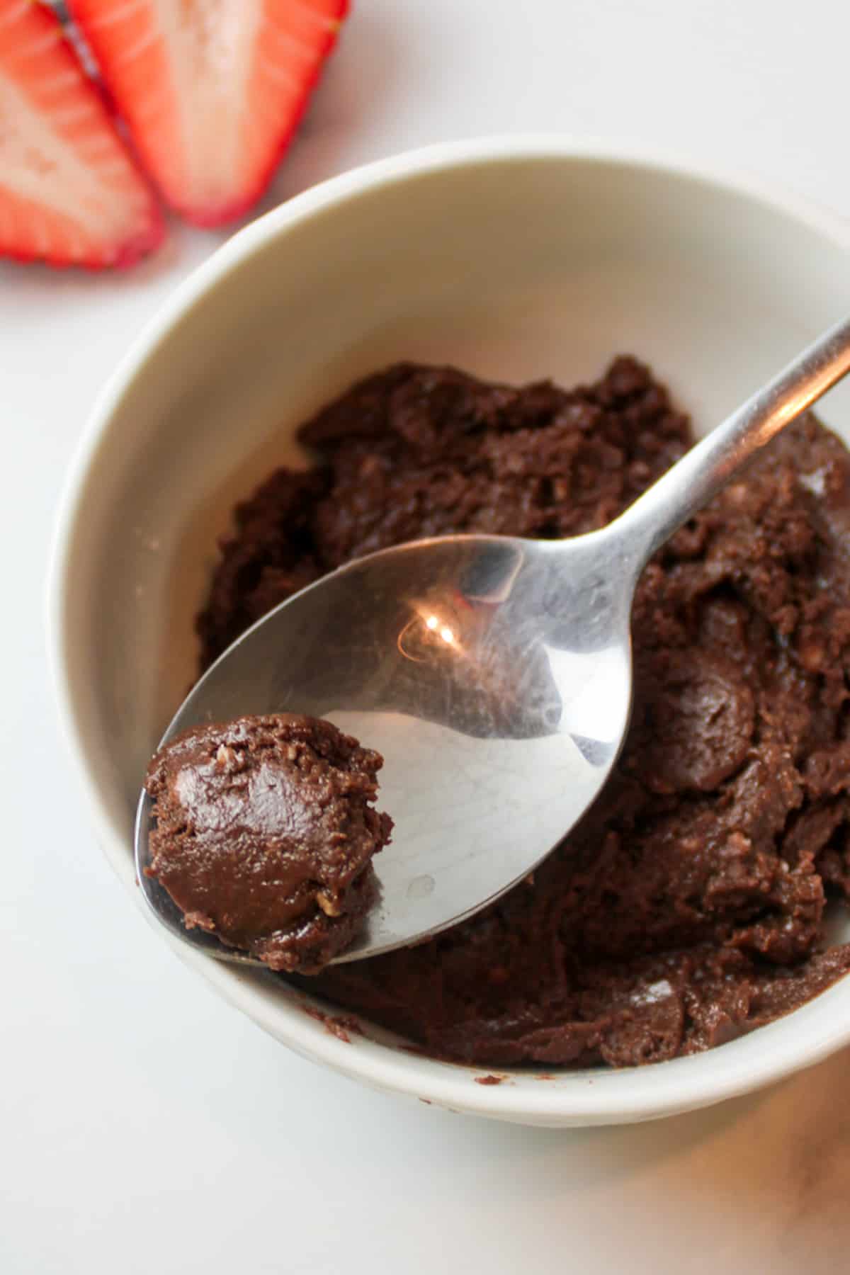 A spoonful of soft chocolate fudge over a bowl with more fudge inside.