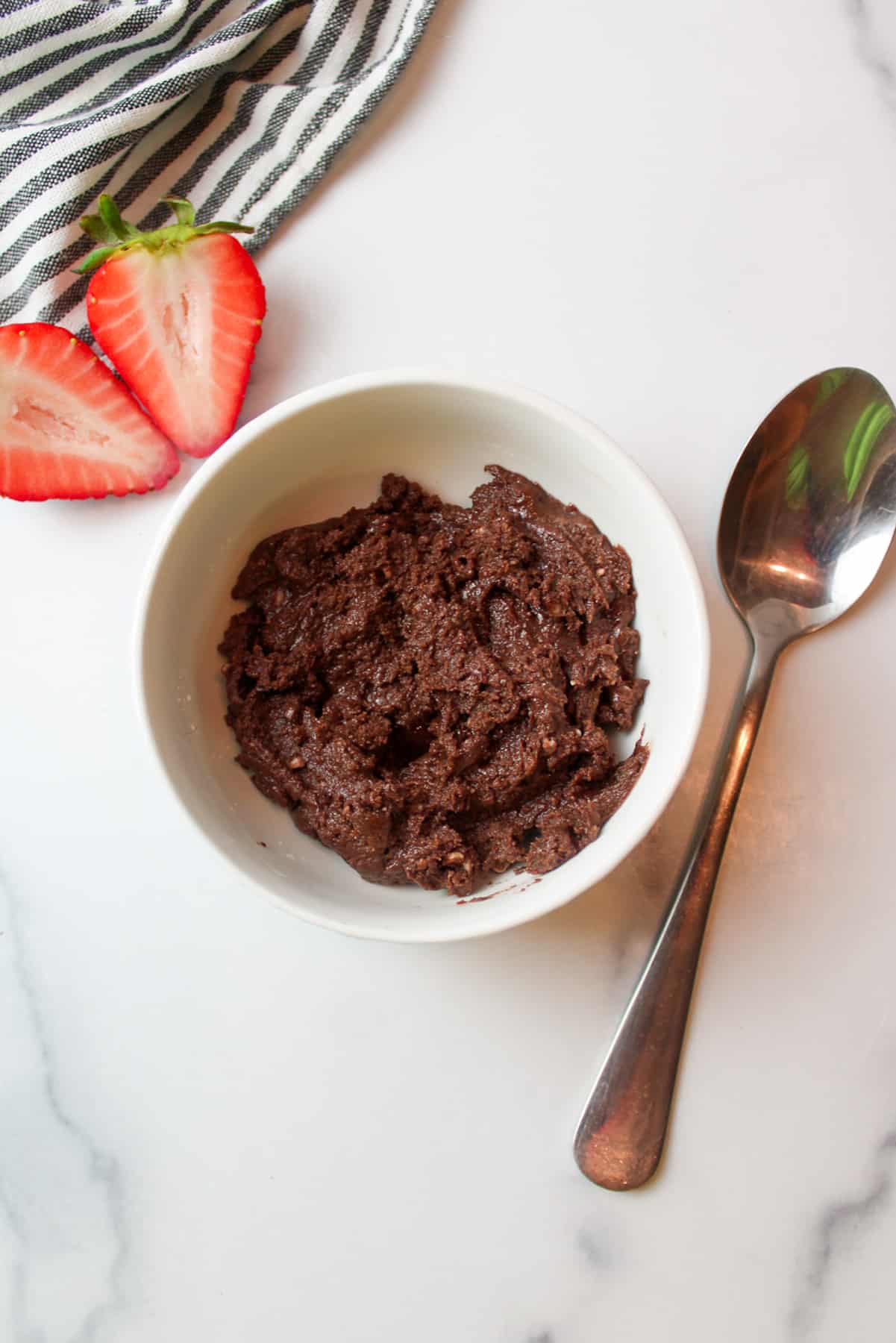 Bowl of soft chocolate fudge with spoon and strawberries on the sides.