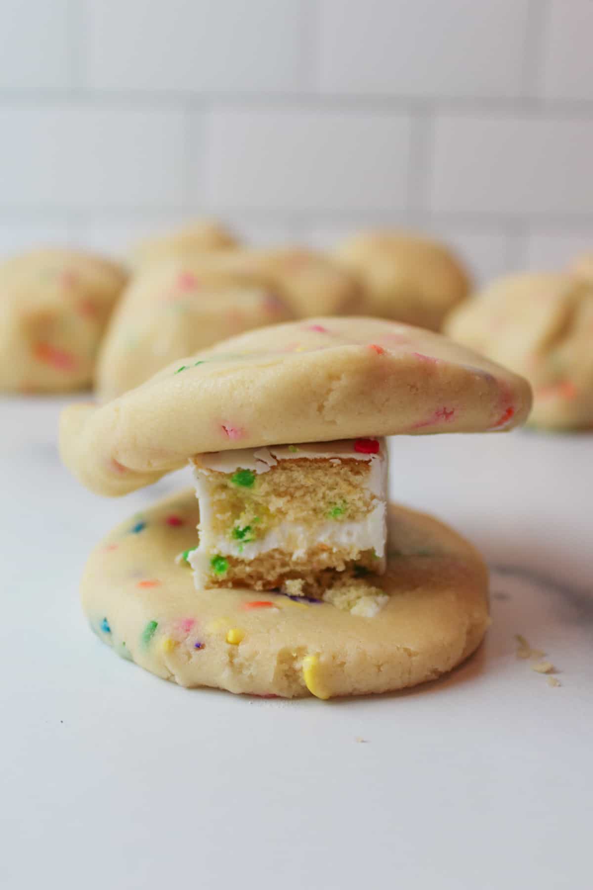 two flattened cookie dough balls with a birthday cake piece sandwiched in the middle