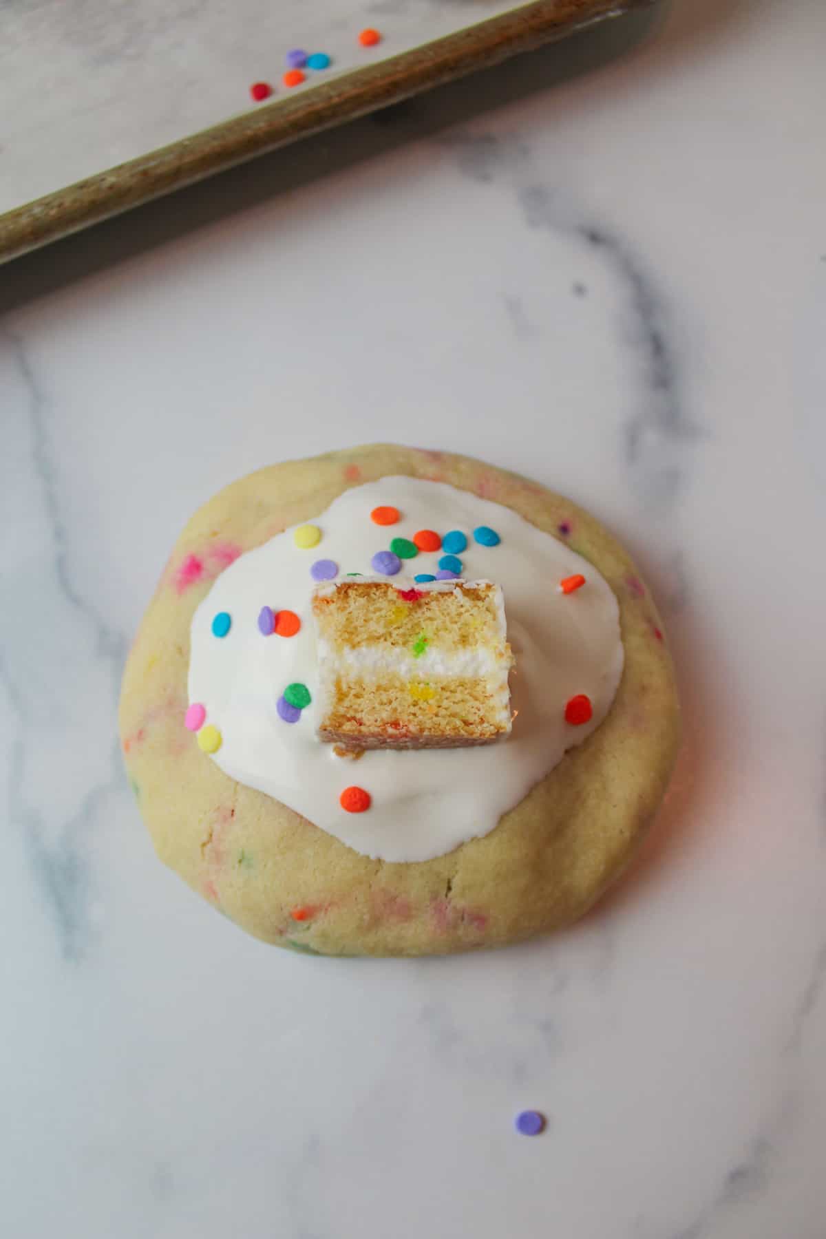 white chocolate topped cookie with sprinkles and a slice of birthday cake on top