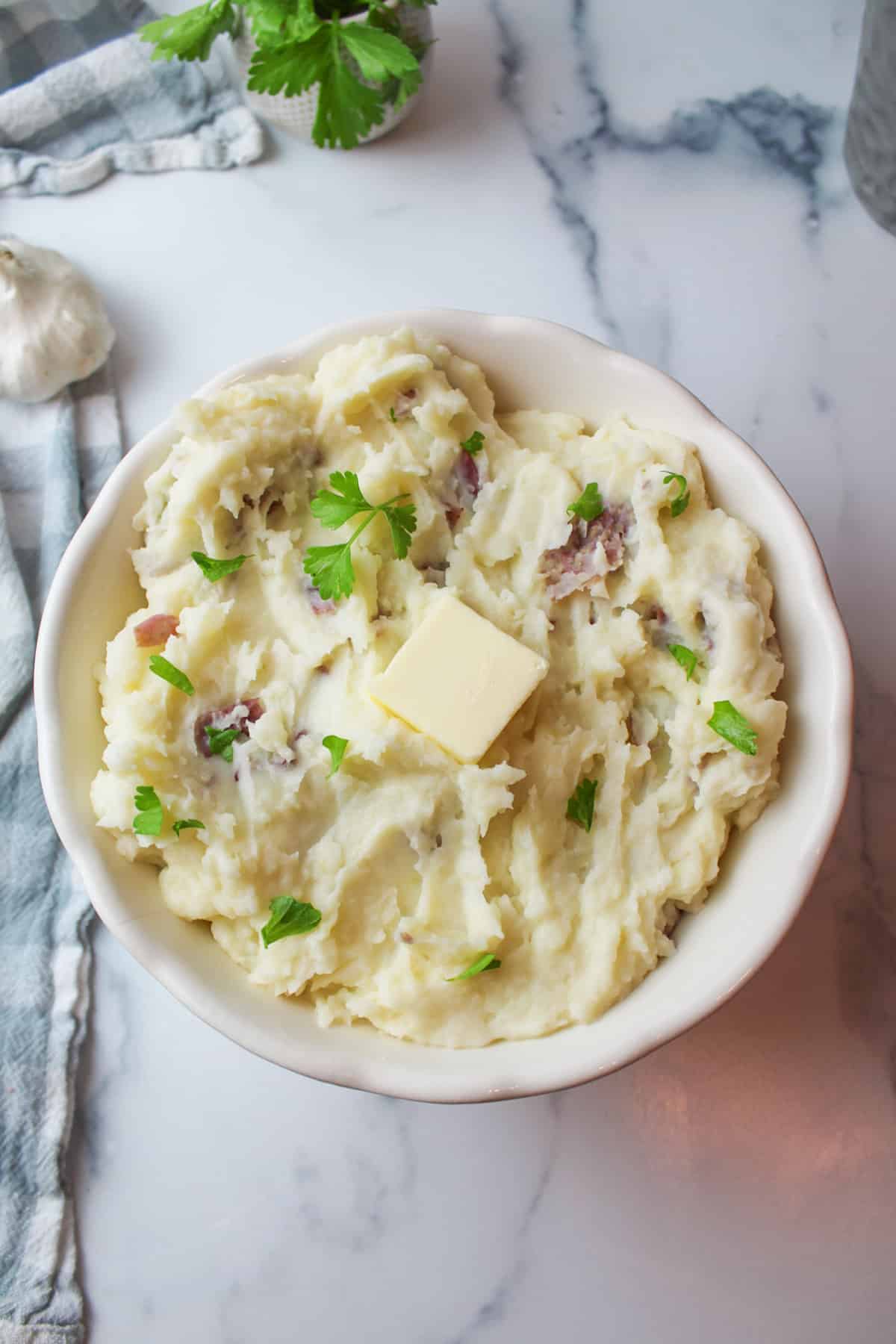 aerial view of creamy mashed potatoes with a pad of butter on top and a head of garlic to the side