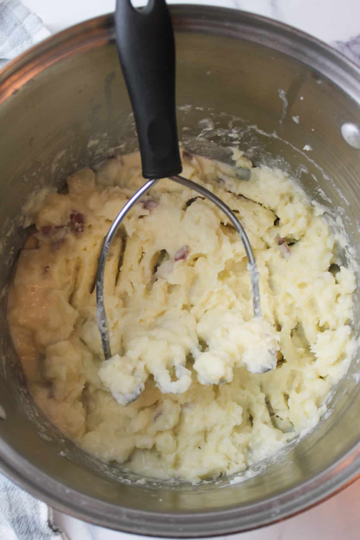 mashed red potatoes in a large pot with a potato masher