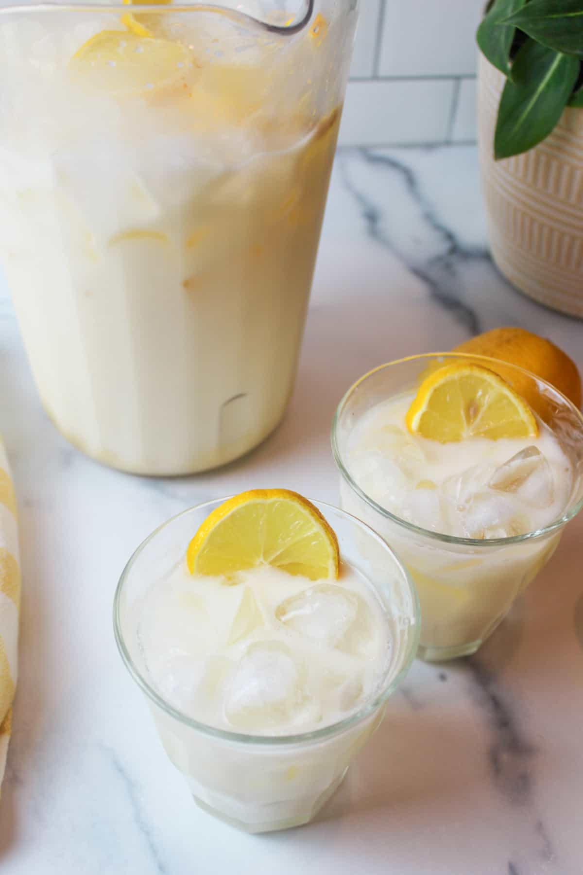 angled view of two glasses full of creamy lemonade with ice and lemon slices