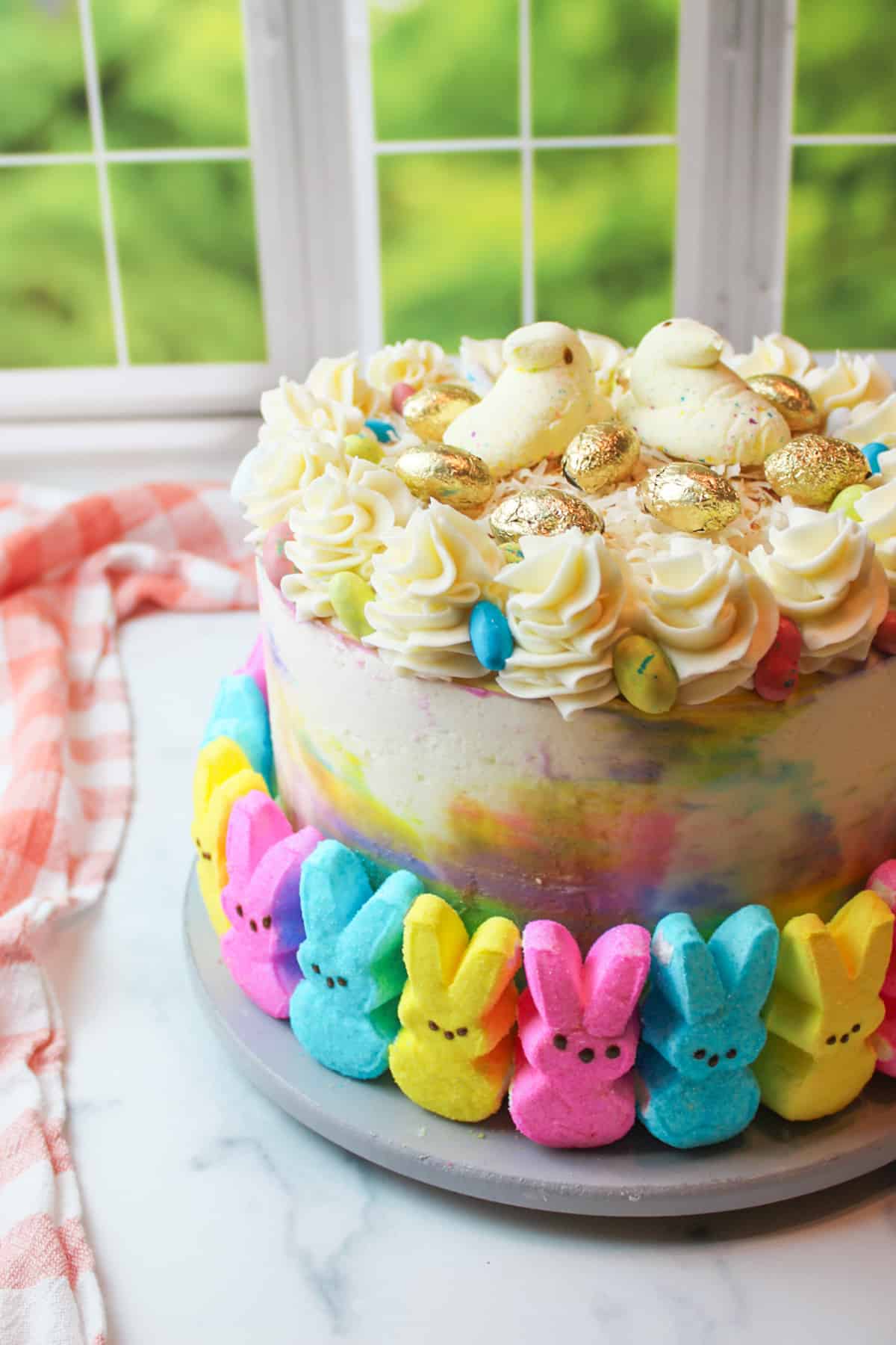 pink blue and yellow peeps around a colorful easter cake topped with shredded cocoanut and golden egg candies.