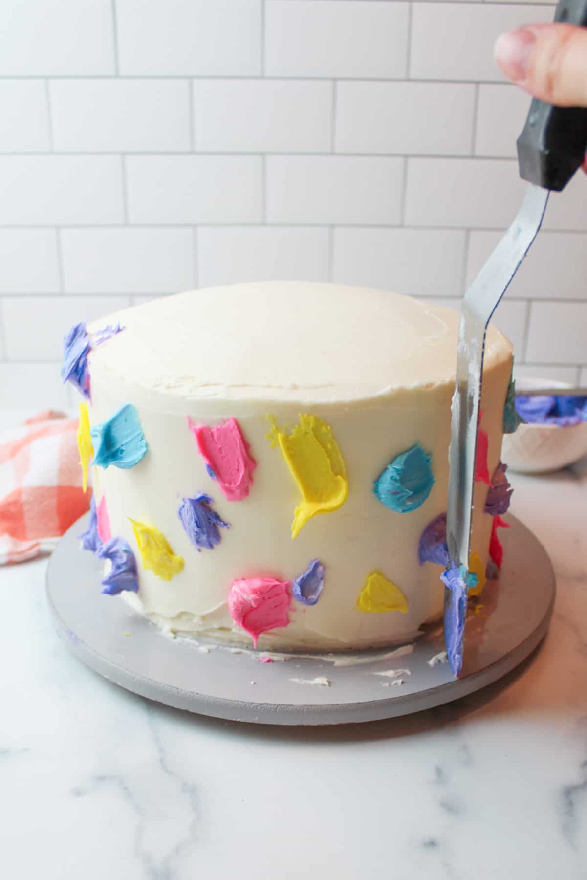 spots of colorful frosting around the sides of an easter cake with a forsting spreader held up against the side of the cake.