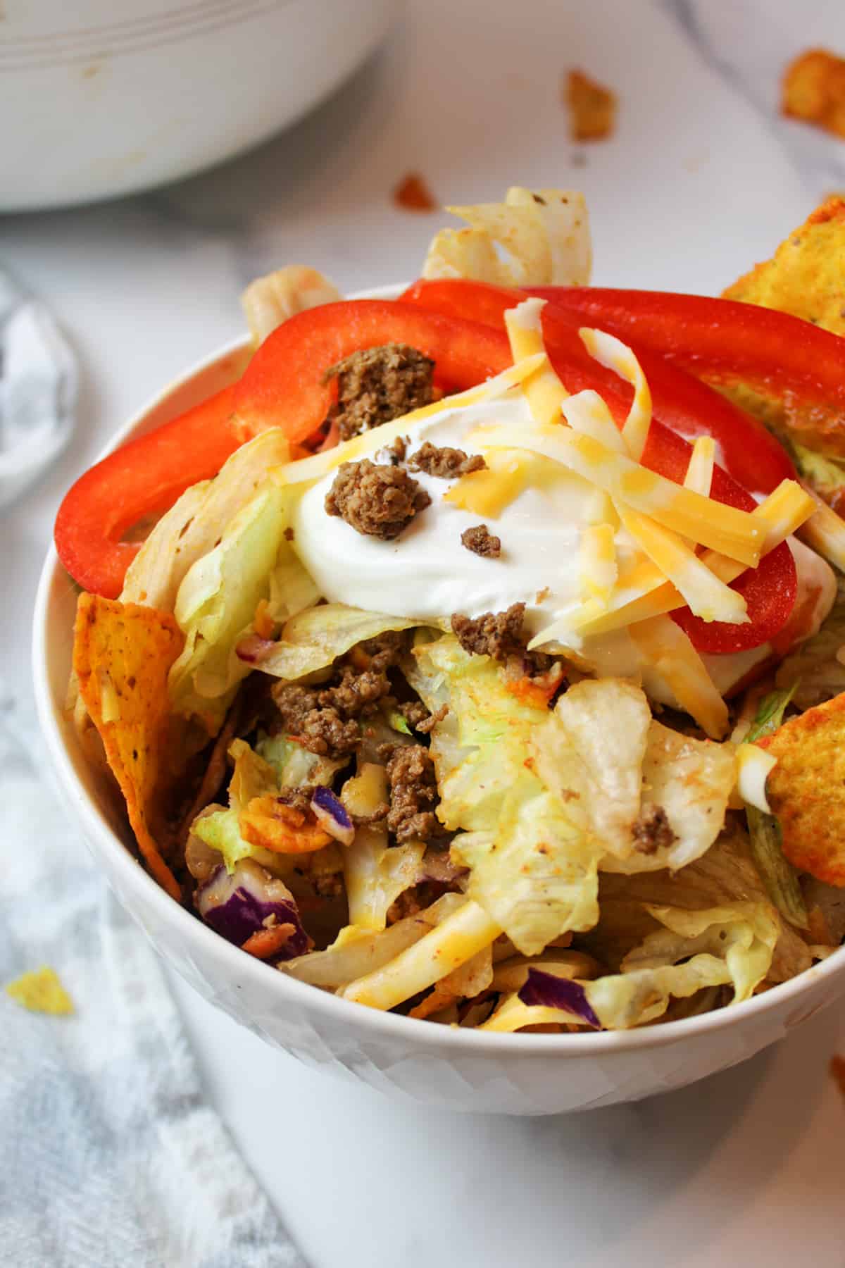 a bowl filled with doritos taco salad and topped with sour cream and red bell pepper