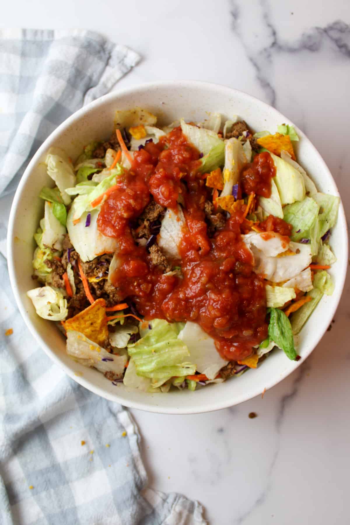 salsa over a salad fillwed with green lettuce, taco meat and crushed doritos chips