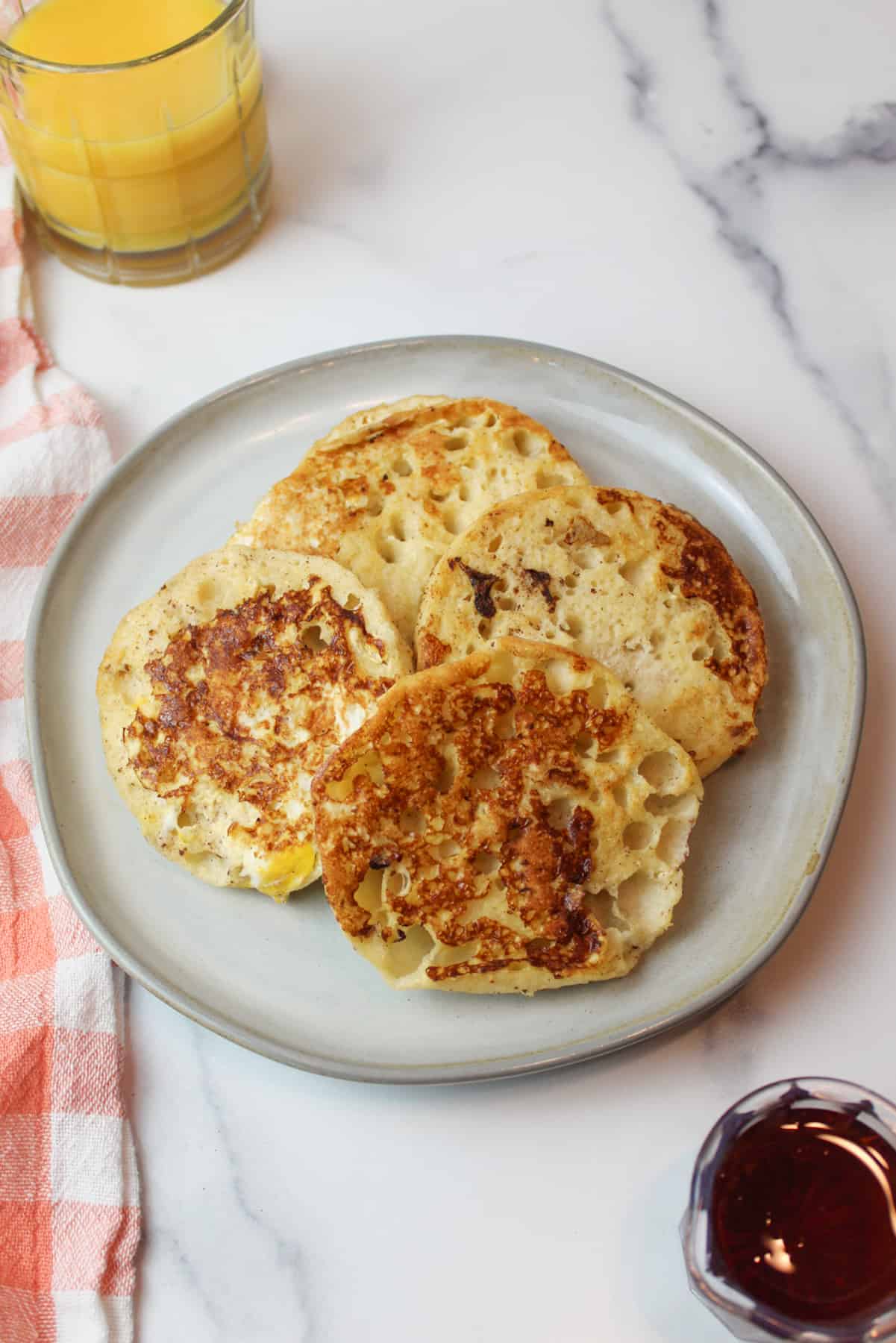 english muffin french toast on a plate with orange juice and maple syrup to the sides