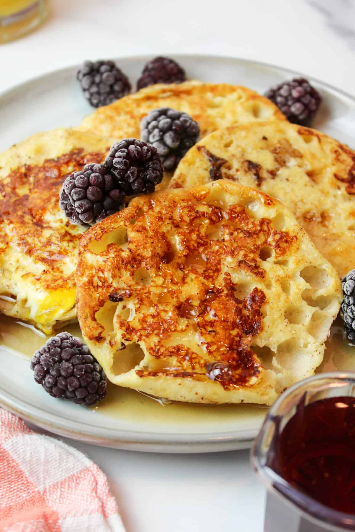 maple syrup and blackberries on english muffin french toast on a plate.