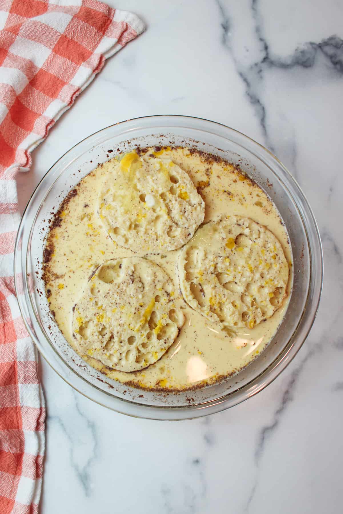 english muffins soaking in french toast egg mixture in pie plate.