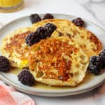 an upclose view of english muffin french toast on a plate with maple syrup and blackberries