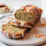 upclose view of sliced fruity pebbles banana bread on a gray plate with scattered cereal around it