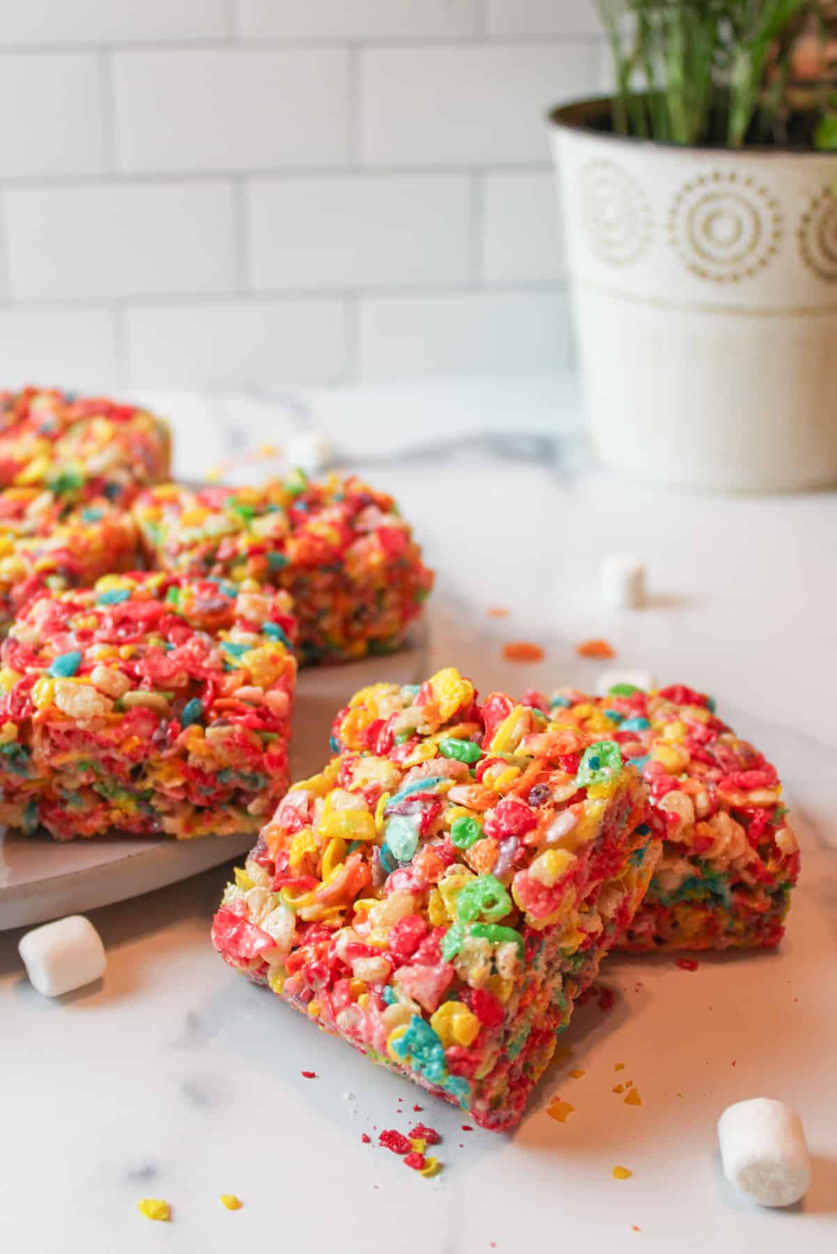 Fruity Pebbles treats cut into squares on and around a round gray plate.