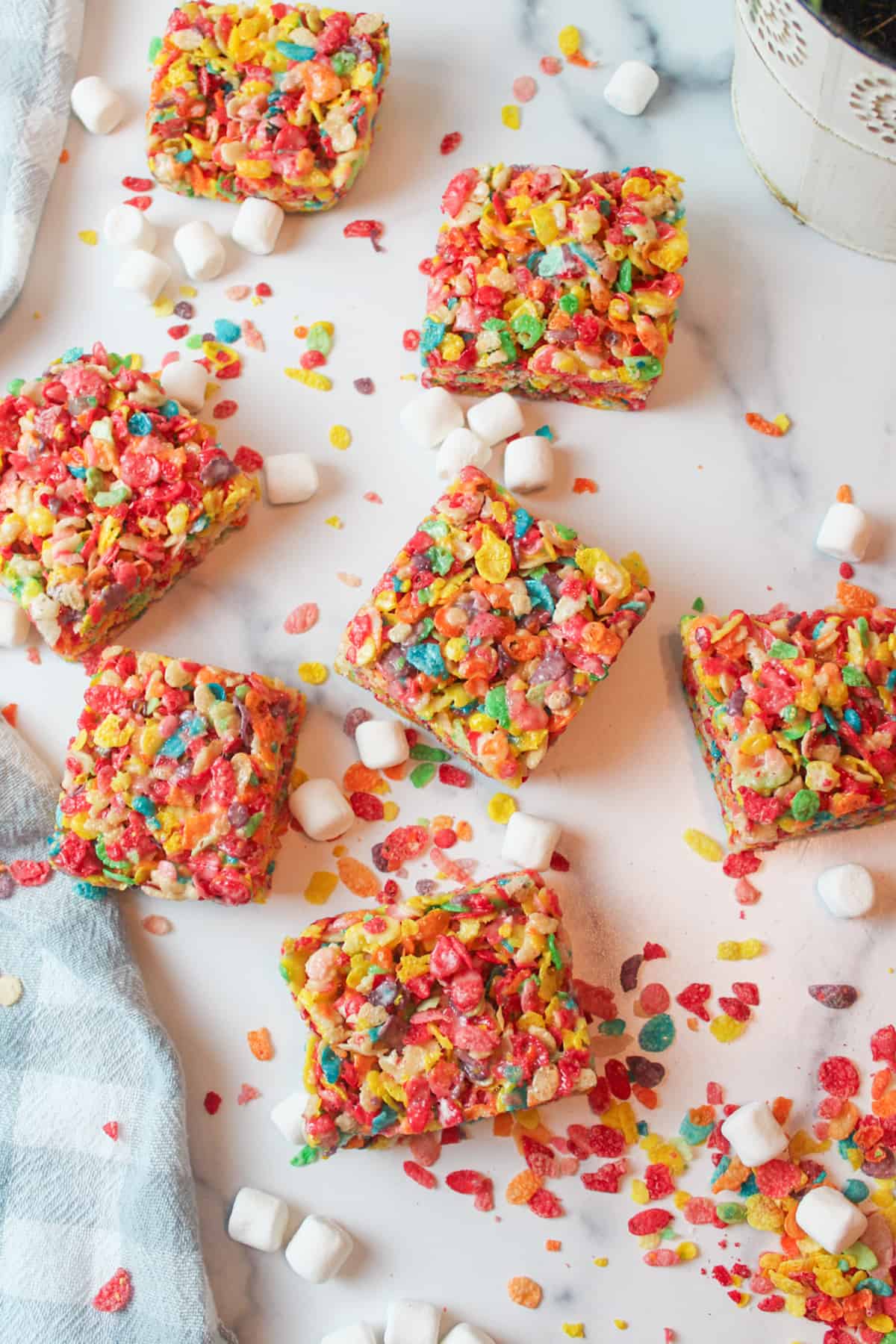 several sliced squares of fruity pebbles treats with scattered cereal and mini marshmallows around them.