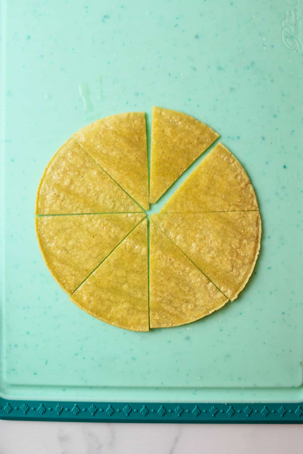 an olive oil coated tortilla chip cut into triangle wedges on a cutting board.