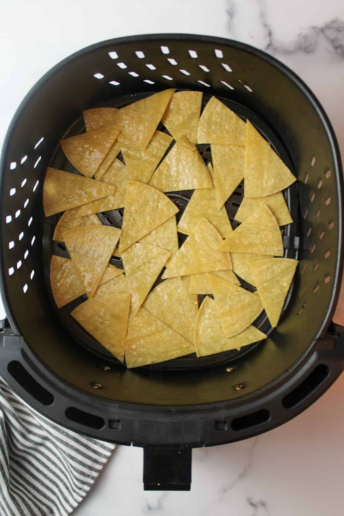 a layer of olive oil coated tortilla chips in an air fryer basket