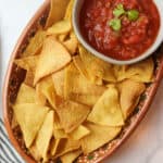 corn tortilla chips in a plate next to a bowl of red salsa.