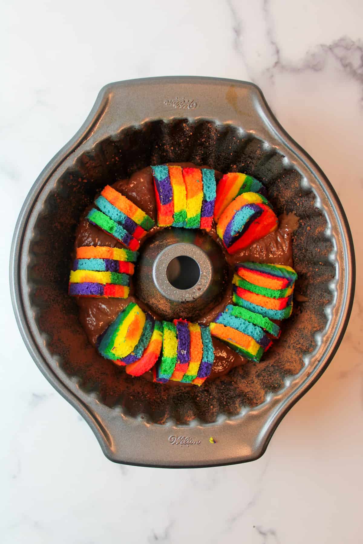 rainbow heart shapes in chocolate cake batter in a bundt pan.