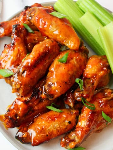 honey buffalo chicken wings on a plate with sliced celery and sliced green onion garnishes