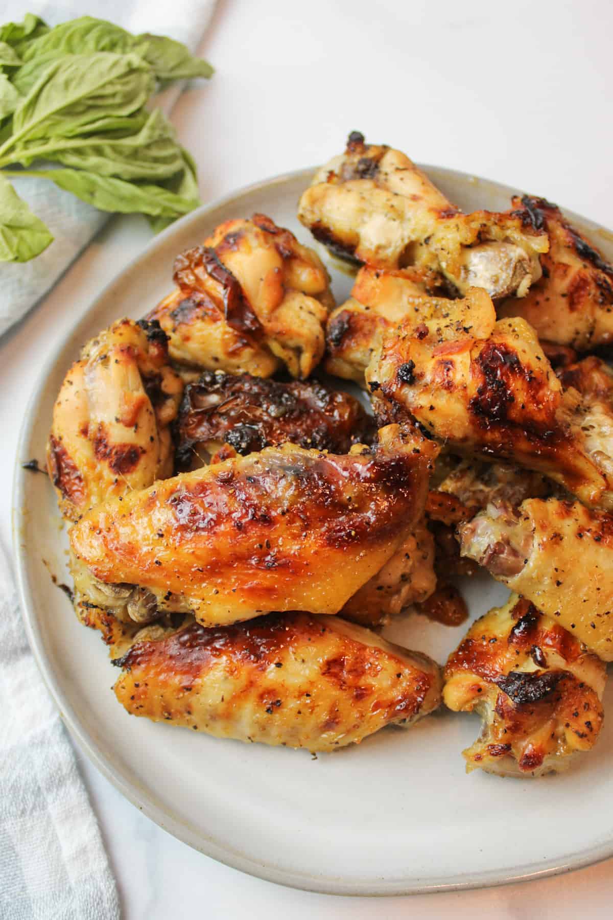 honey lemon pepper wings on a plate with fresh green herbs to the side in the background