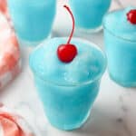 blue kool aid slushie in a cup topped with a red cherry.