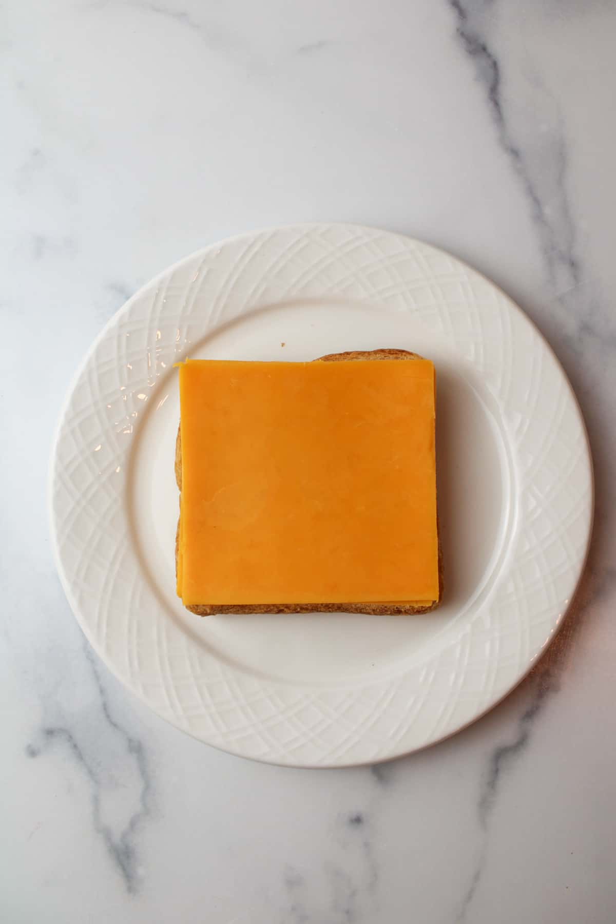 slice of cheddar cheese on toast on a white plate.