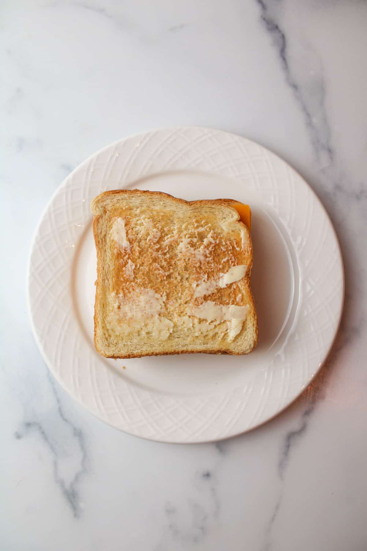 buttered slice of toast sandwich with cheese in the middle on a white plate.