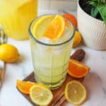 an upclose view of orange lemonade in a glass with sliced lemons and oranges