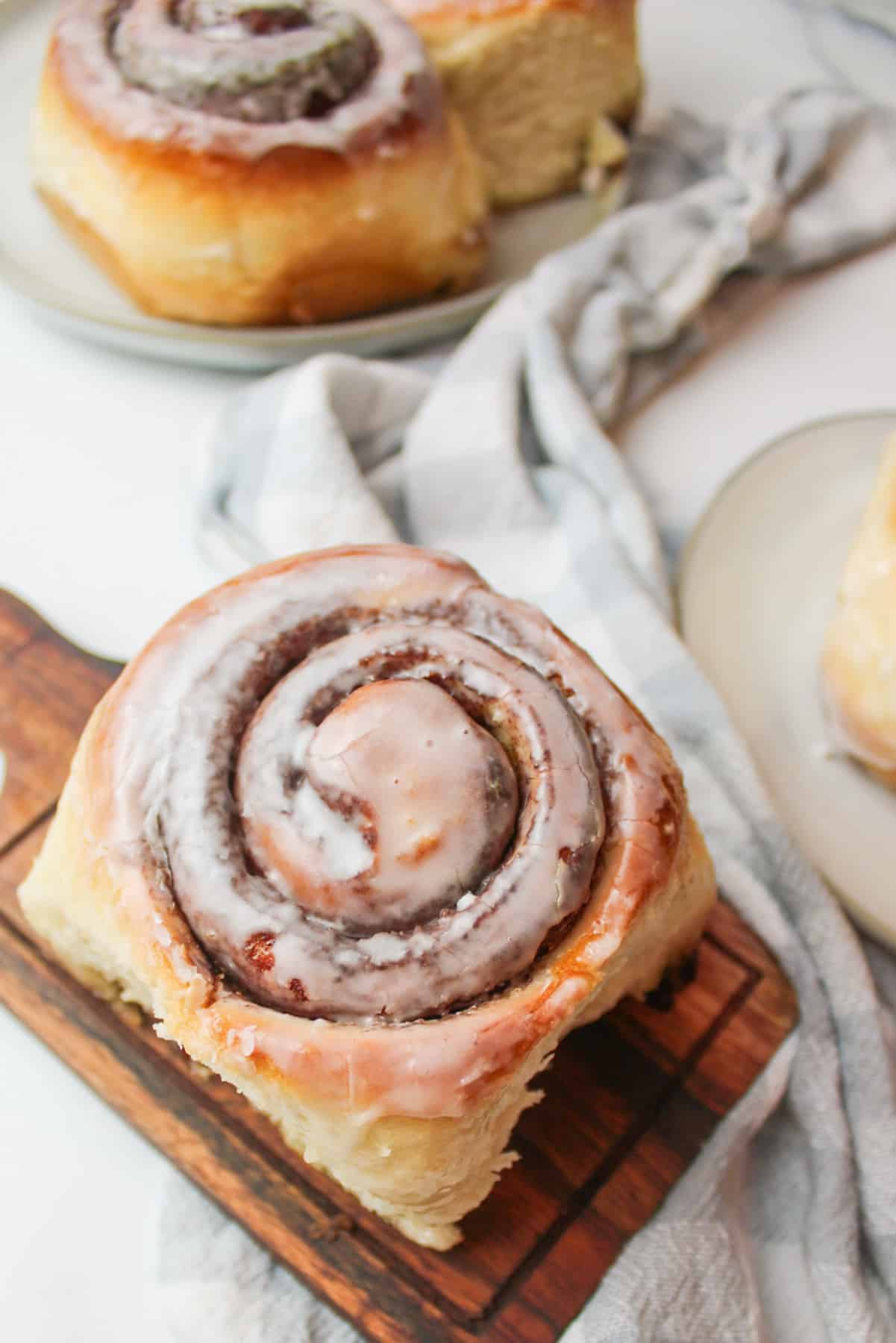 an iced cinnamon roll on a wooden cutting board.