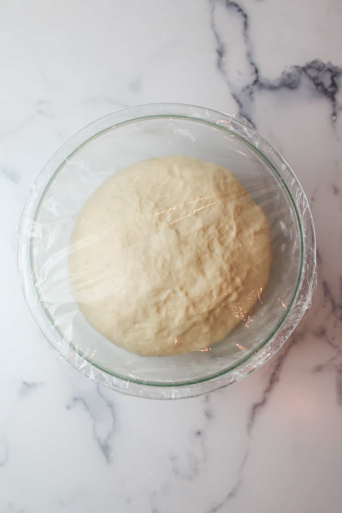 proofed dough in a mixing bowl covered in plastic wrap.