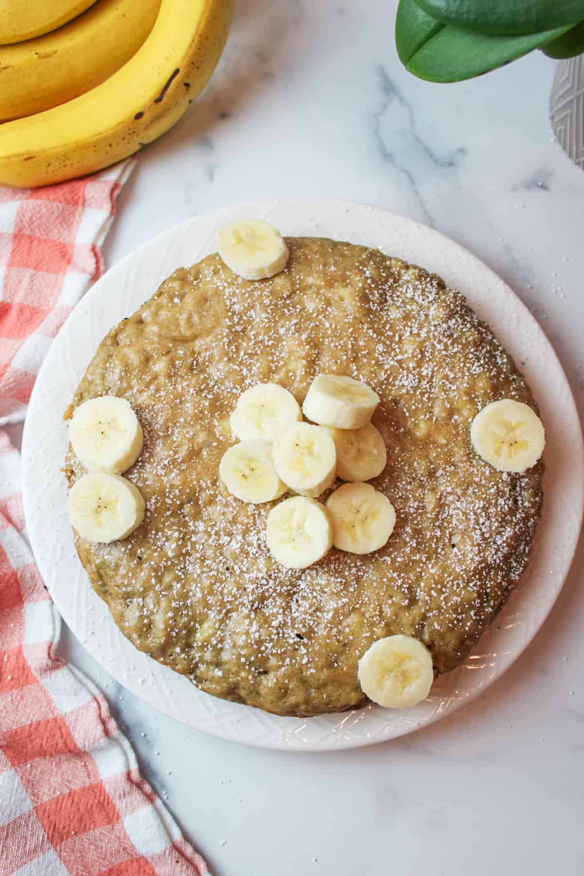 aerial view of powdered sugar dusted stovetop banana bread on a plate with fresh banana slices