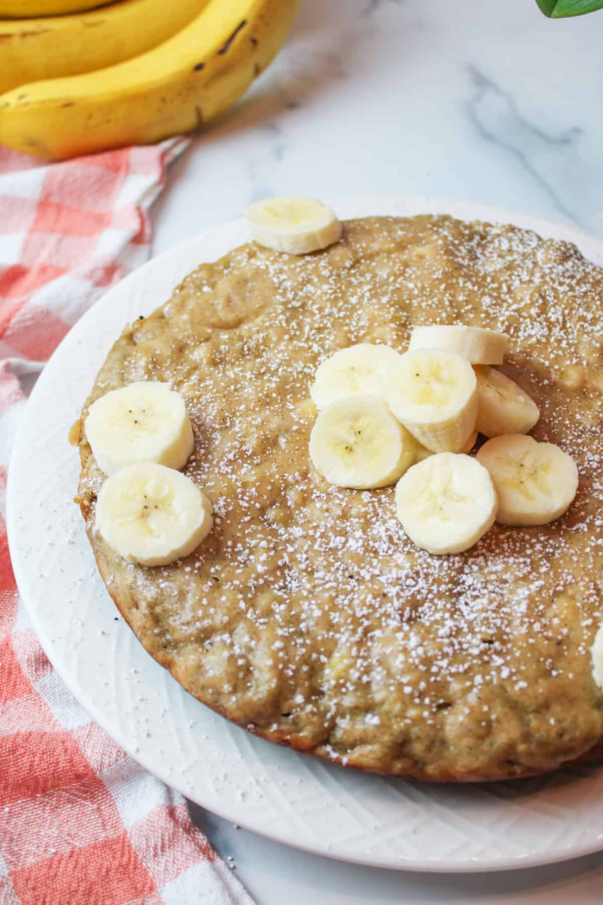 Stovetop banana bread on plate, powdered sugar, sliced ripe bananas garnish.