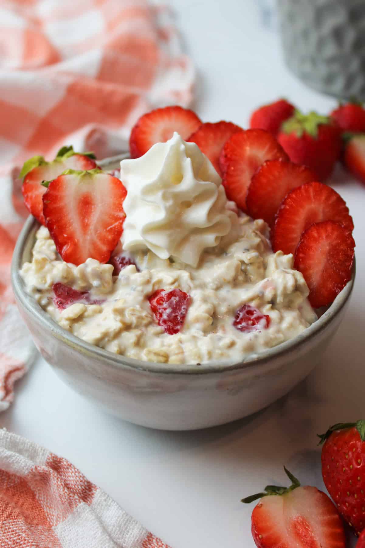 a bowl of strawberries and cream overnight oats with sliced fresh strawberries and whipped cream on top