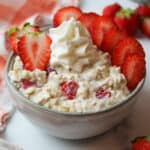 a close up of strawberries and cream overnight oats in a bowl with toppings