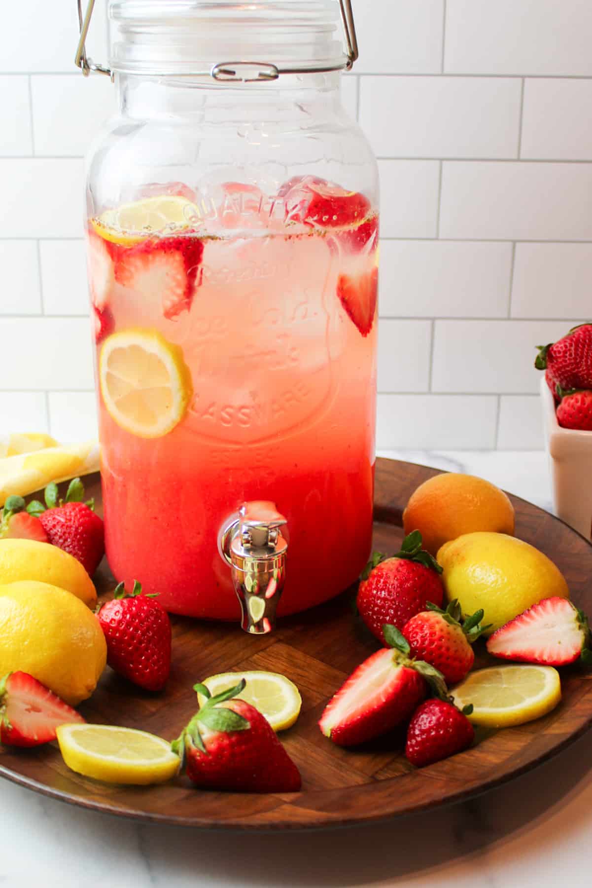 A pitcher of strawberry lemonade on a tray with strawberries and lemons.