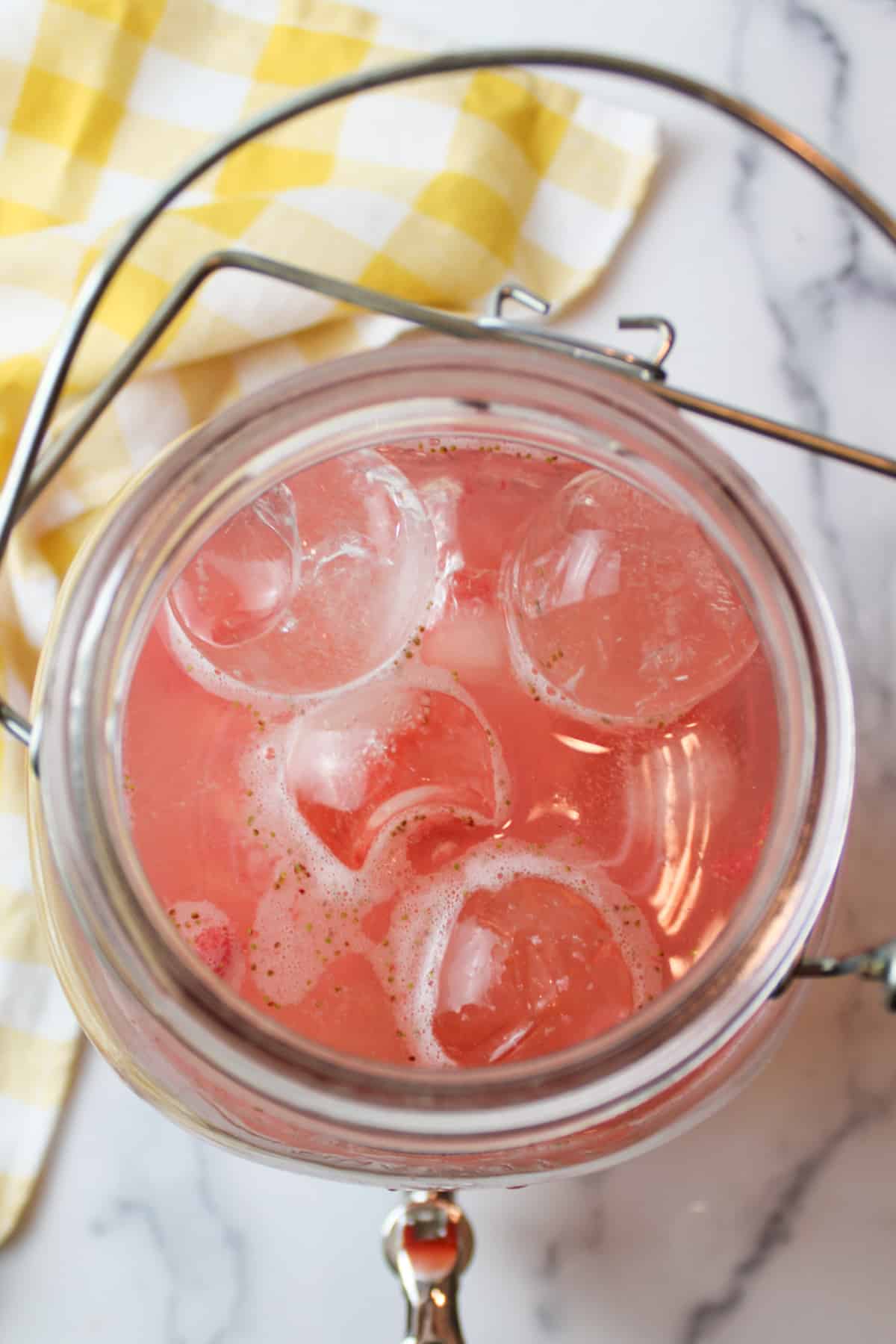 water added to strawberry lemonade and ice in a glass pitcher.