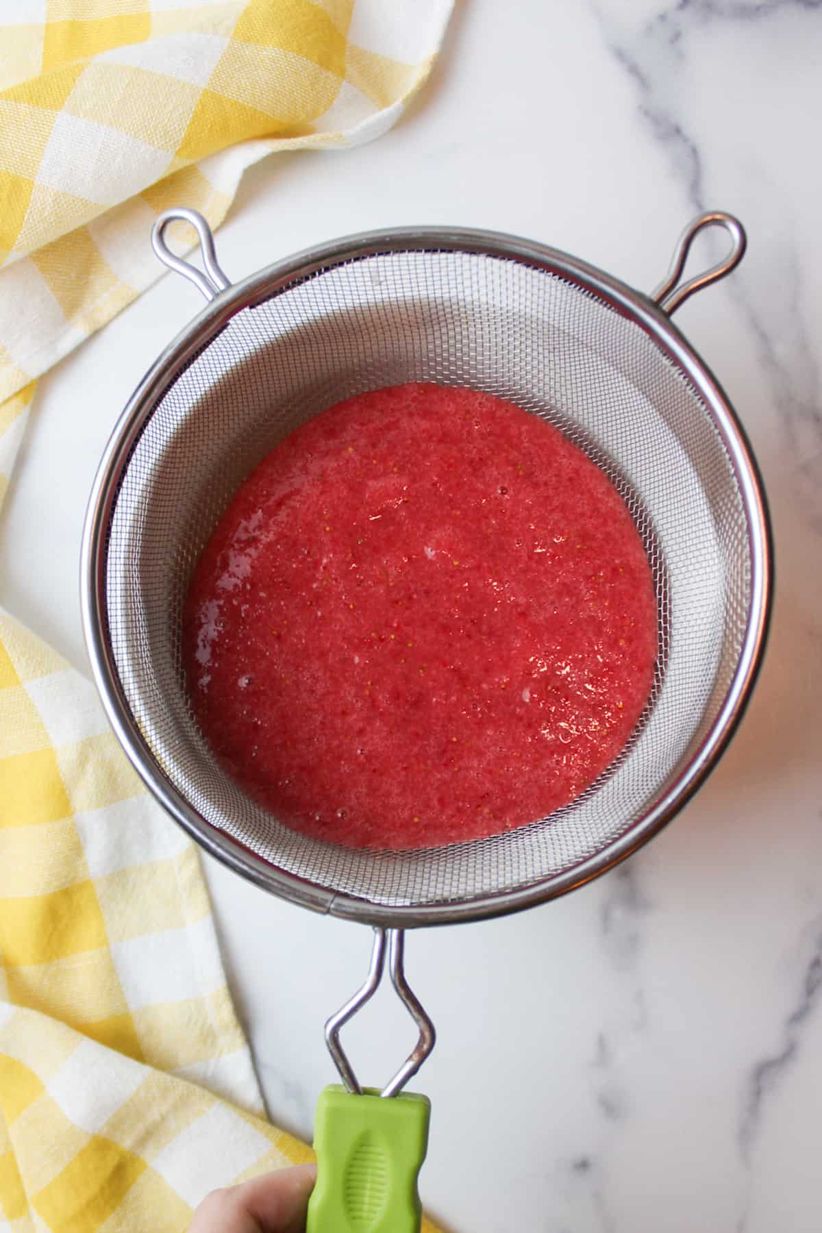 strawberry puree in a sieve over a bowl.