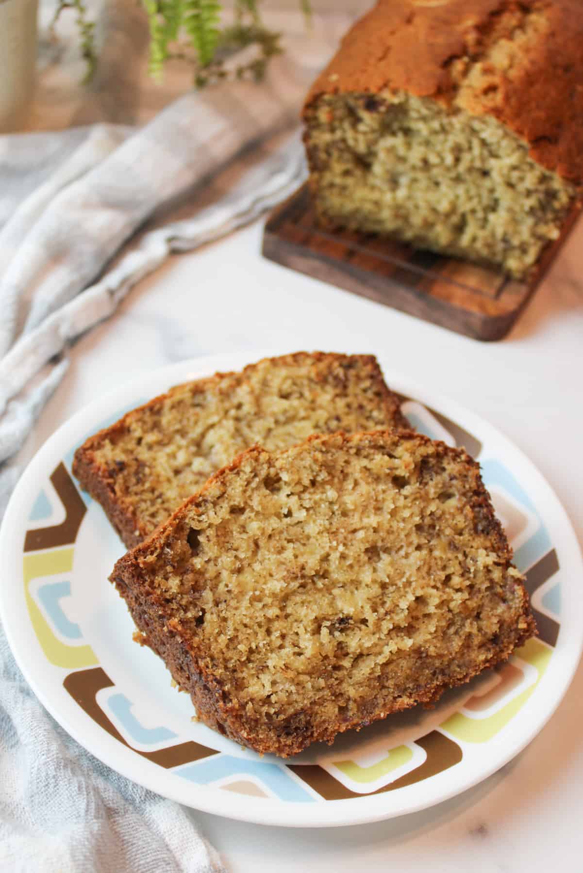 two slices of banana bread on a small plate with more on a wooden cutting board in the background