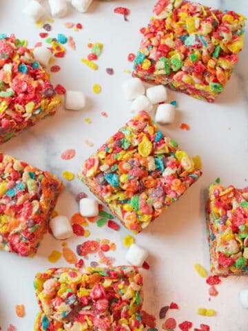 sliced squares of fruity pebbles treats with scattered cereal and mini marshmallows around them.