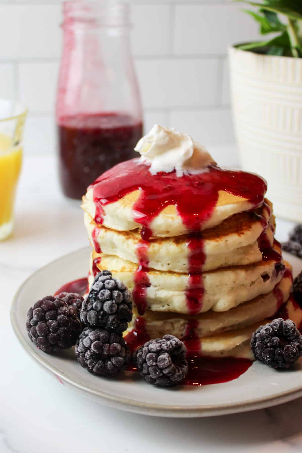 a stack of pancakes topped with berry syrup and whipped cream with frozen blackberries to the sides