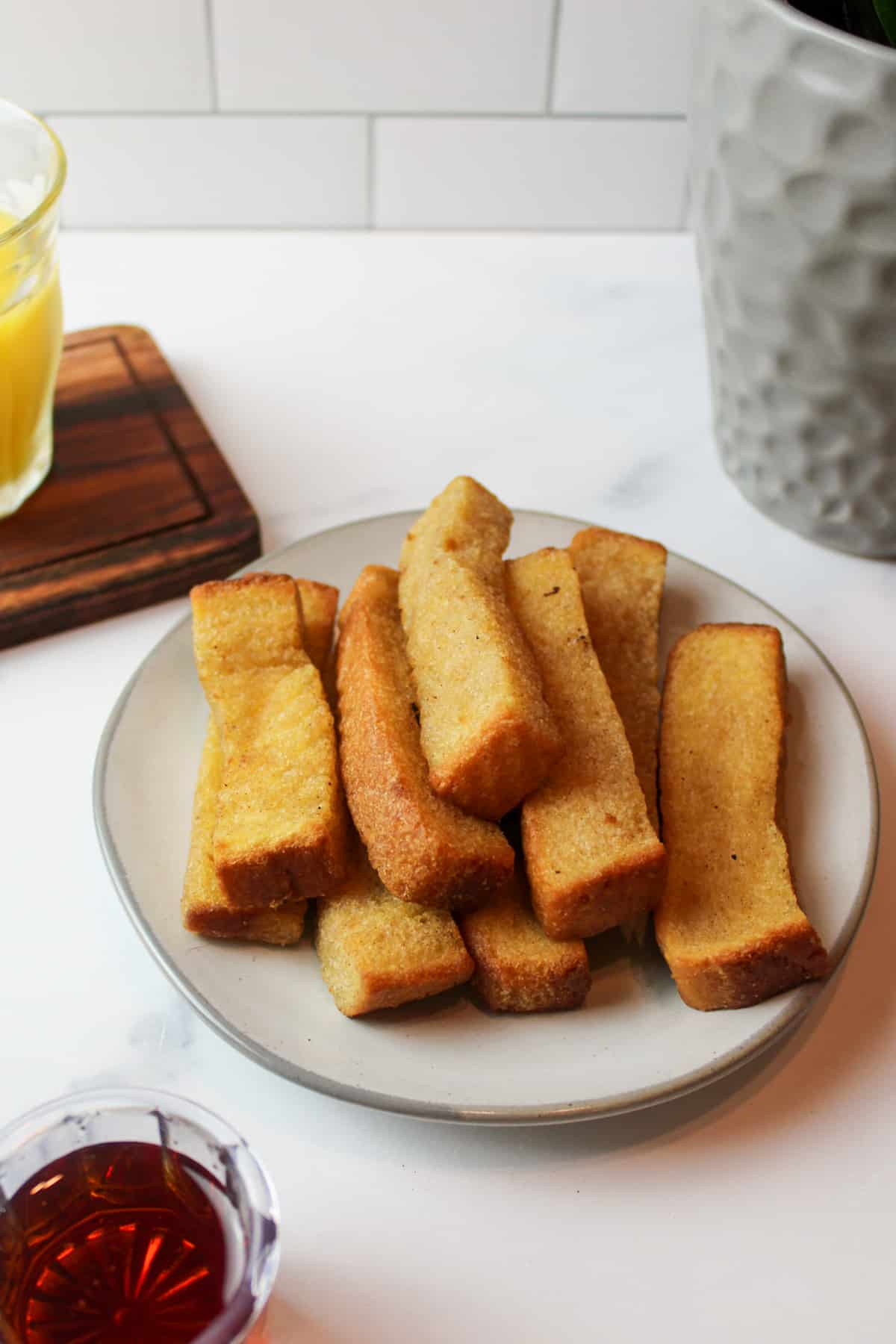 a plate with a pile of french toast sticks and a container of maple syrup in front